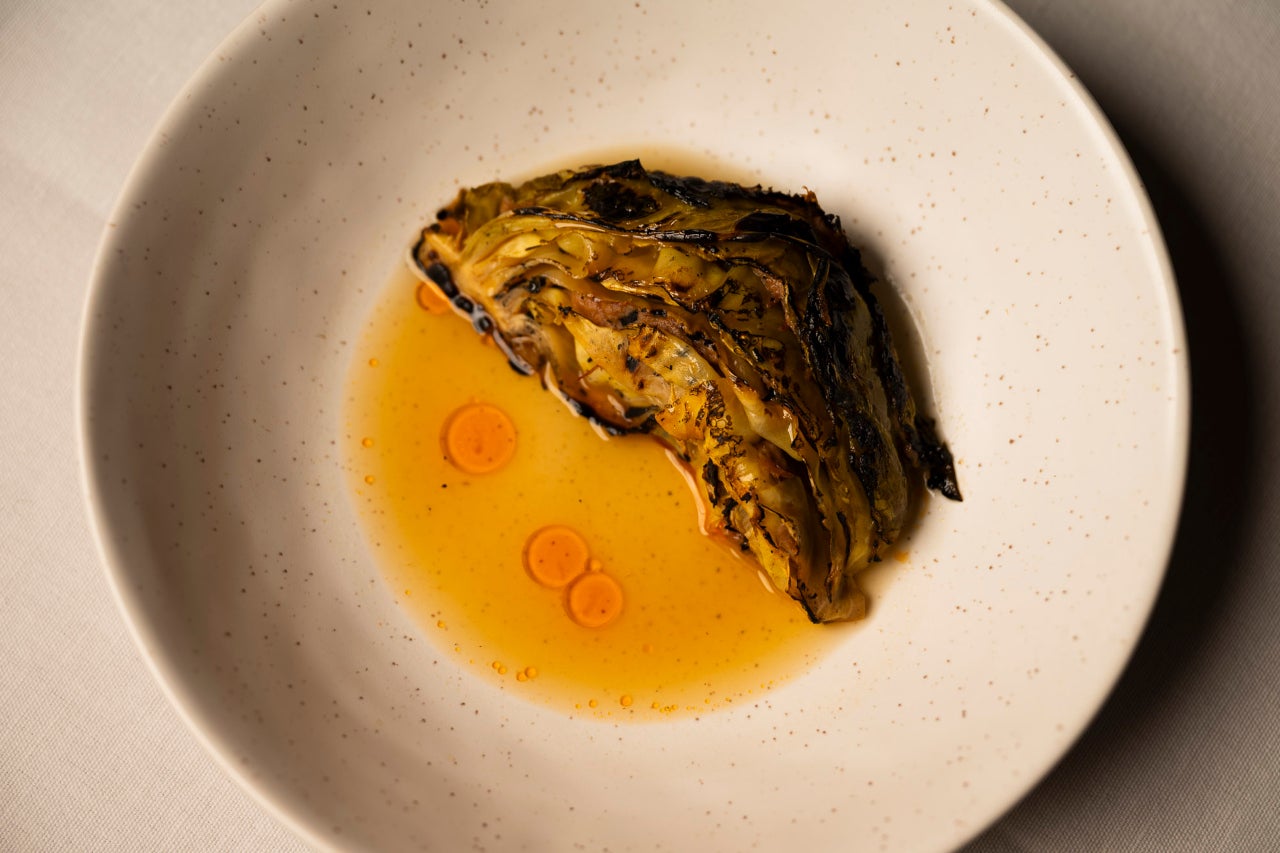 Os pratos de vegetais estão entre os mais surpreendentes. Um exemplo é esta couve grelhada, recheada com feijão e servida com caldo de porco