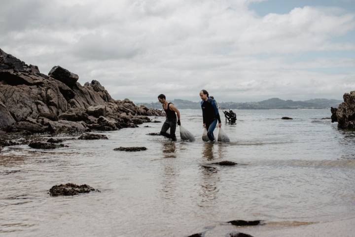 Sergio y Óscar, de Mar de Ardora, ayudan a sacar del agua los sacos que Alberto ha arrastrado hasta la orilla de la playa, en Galicia.