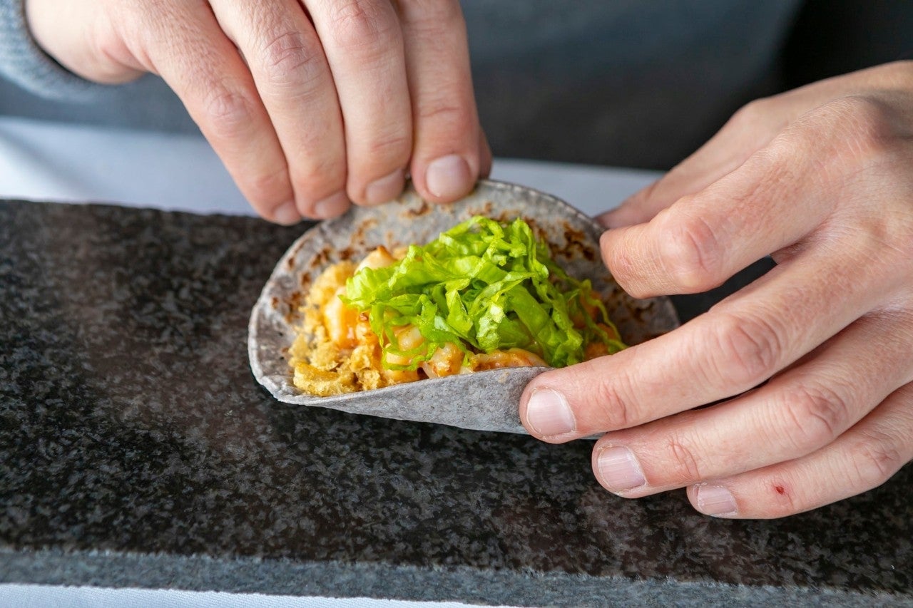 El taco de camarón emulsionado en chiles se sirve con crema de fréjol negro, corteza de cerdo y virutas de lechuga.