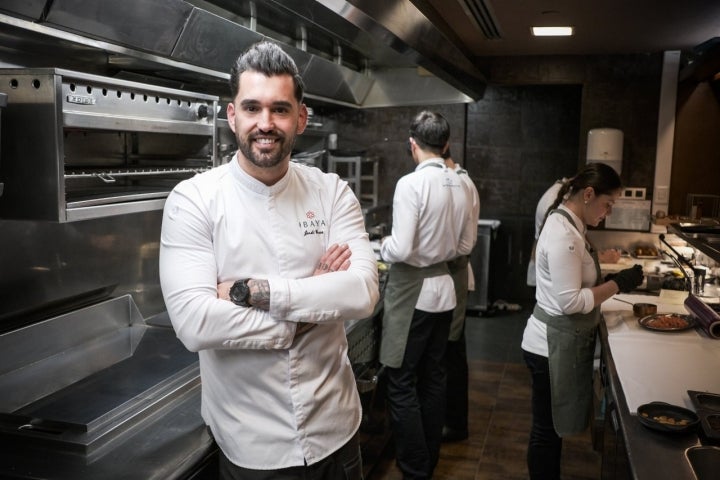 Retrato de Jordi Grau en la cocina con parte de su equipo trabajando detrás.