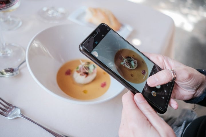 Una mujer fotografía un plato de Vieira a la plancha con una crema de calabaza.