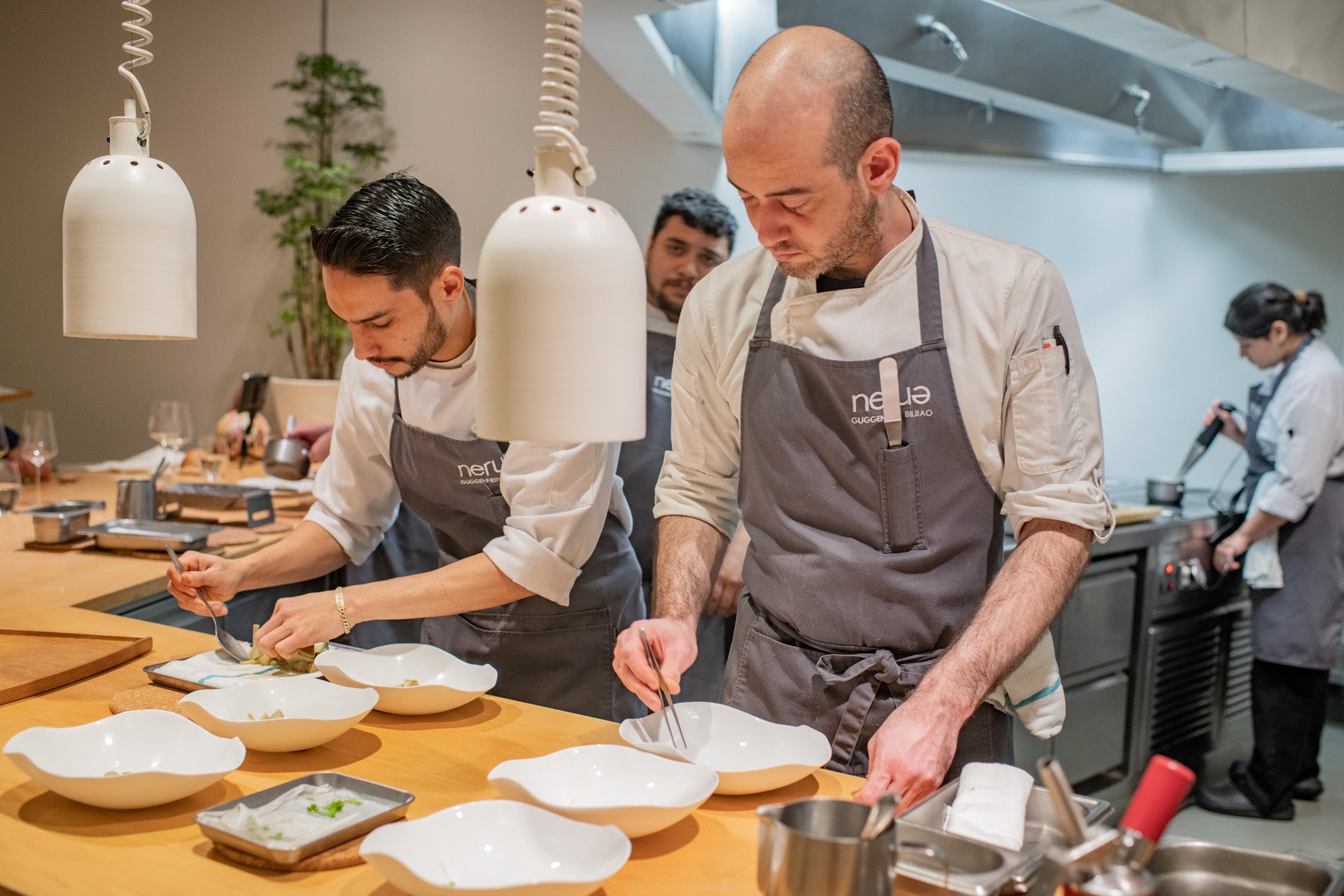 Dos jóvenes trabajan en la cocina del restaurante con Toño, jefe de cocina, atrás.