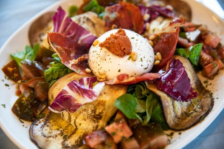 Ensalada de burrata con berenjena, canónigos y piñones con salsa de tomate seco y anchoa.