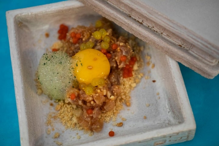 Tartar de ijada de lecha con huevo semi curado en soja, curry verde, apio, cítricos, perlas de tomate, crumble de almendra y aceite de carbón.