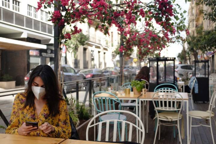 Una mujer mira el móvil en la terraza a pie de calle de Pipa & Co rodeada de las flores que dan sombra a la terraza.