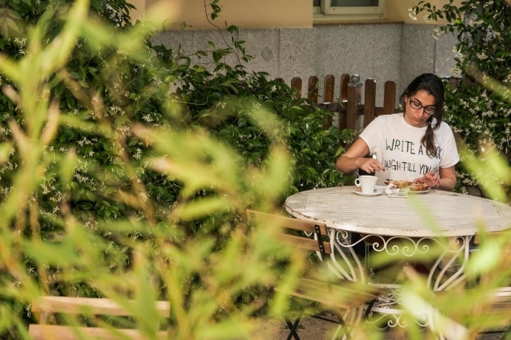 Una mujer toma un desayuno en la terraza del Café de l'Institut Français rodeada de su vegetación.