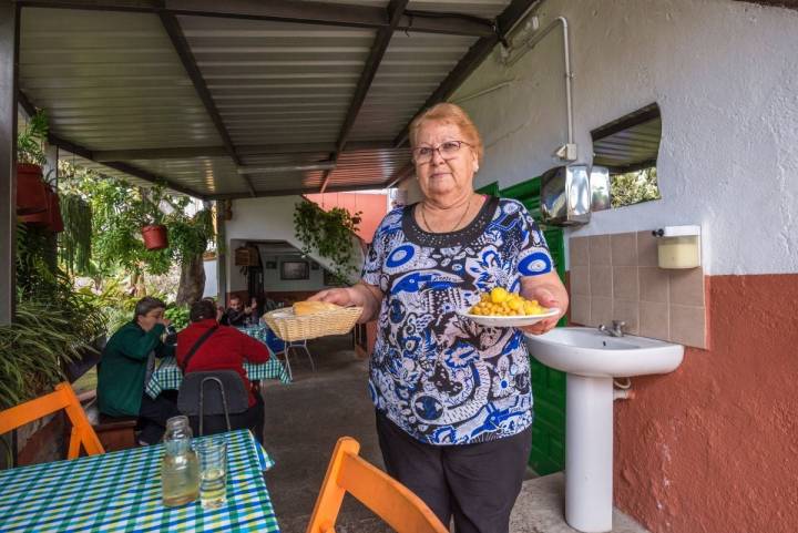 Una de las antiguas propietarias del guachinche Las Galanas, en Tenerife, sirve en una mesa del patio, un plato de garbanzas junto al vino.