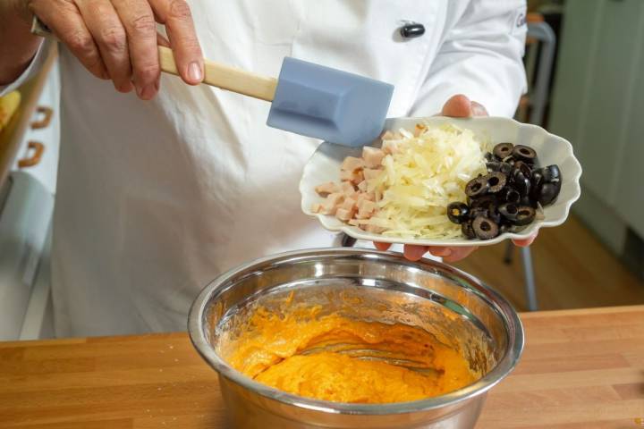 Echando las aceitunas a la masa del bizcocho de fiambre, aceitunas y queso con pimentón.
