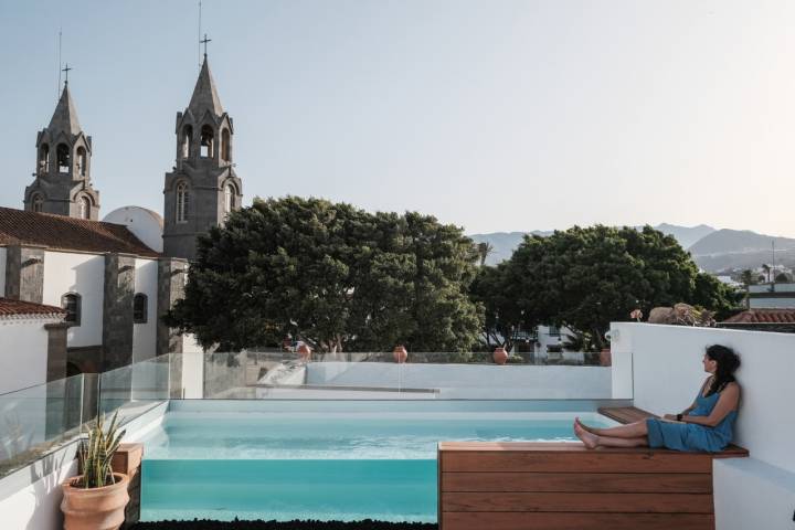 Una mujer sentada en la piscina de la azotea del hotel con la iglesia al fondo.
