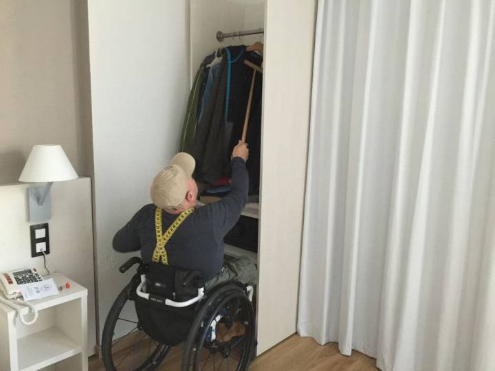 Hombre en silla de ruedas en una habitación accesible colgando ropa en un armario