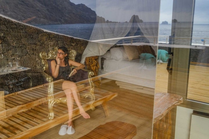 En la ventana de la terraza de la suite del Hotel Puntagrande se aprecia el reflejo del mar y dentro una mujer pensando.