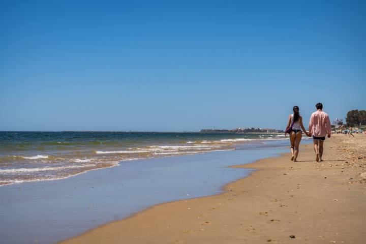 Dos personas paseando por la orilla de la playa de Islantilla (Huelva)