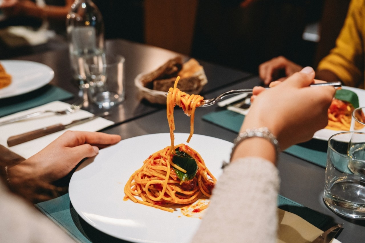 Close-up of a woman twirling spaghetti with tomato sauce and basil onto her fork in a restaurant