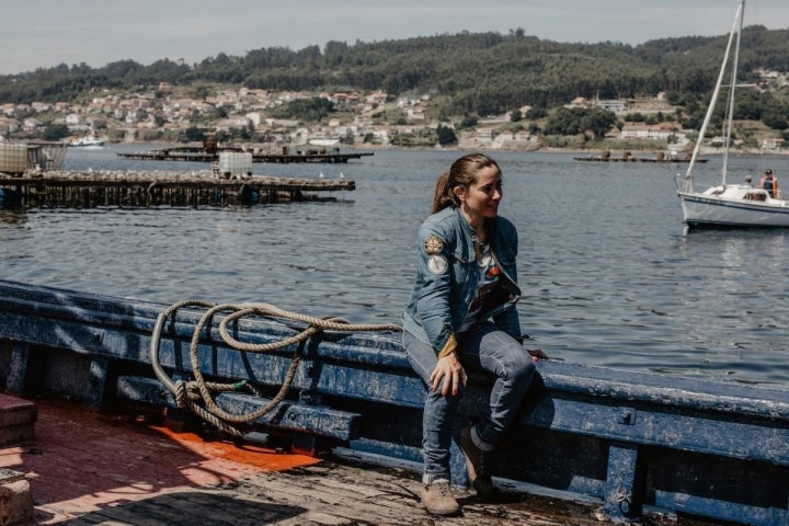 La periodista motera sobre una de las barcas con las bateas tras de sí y, al fondo, Combarro.