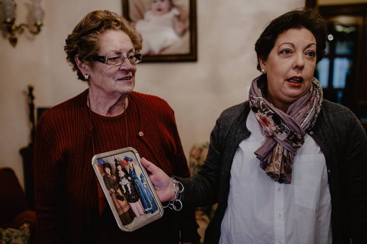 María y Gloria, en el salón de esta última, muestran una foto con las cuatro generaciones de viudas.