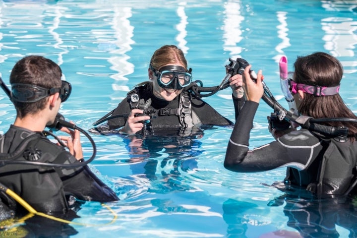 Scuba dive training in the pool with a smiling instructor teaching two students