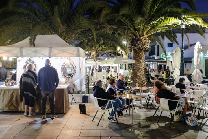 Una terraza llena de gente al lado de uno de los puestos del mercadillo nocturno.