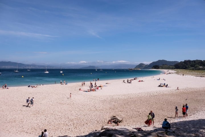 Varias personas toman el sol o se bañan en la Playa de Rodas.