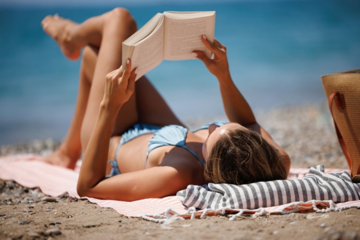Relaxed woman enjoying book on beach by the sea