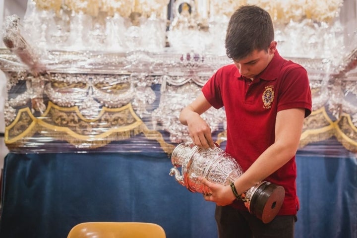 Uno de los jóvenes de la Hermandad de la Sed da lustre a la plata del palio de la Virgen de Consolación.