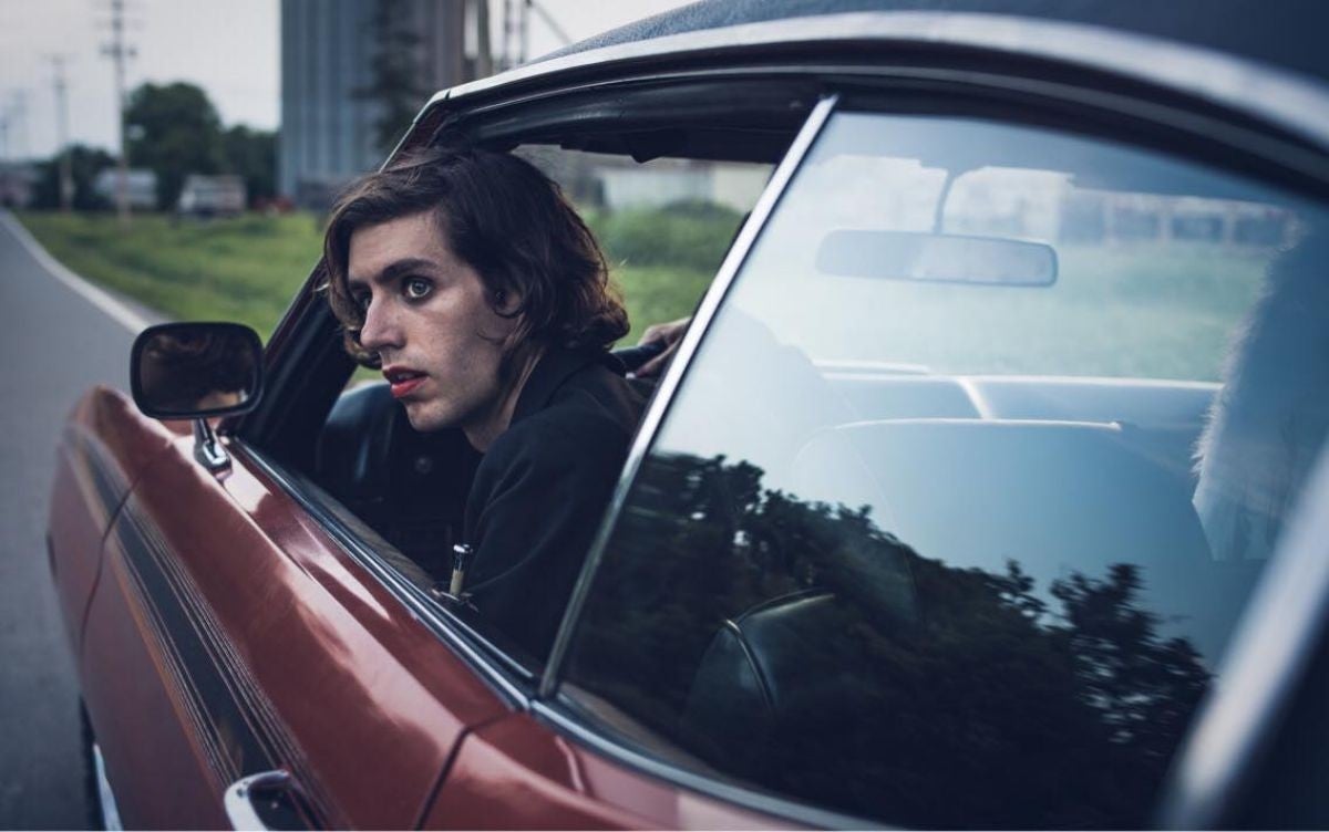 Ezra Furman asomado por la ventanilla de un coche que conduce.