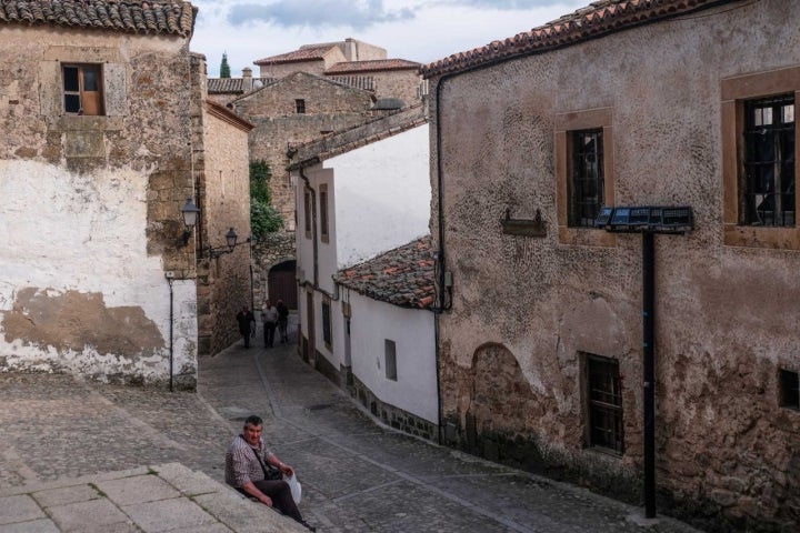 Calle empedrada de la zona amurallada de Trujillo con señor sentado.