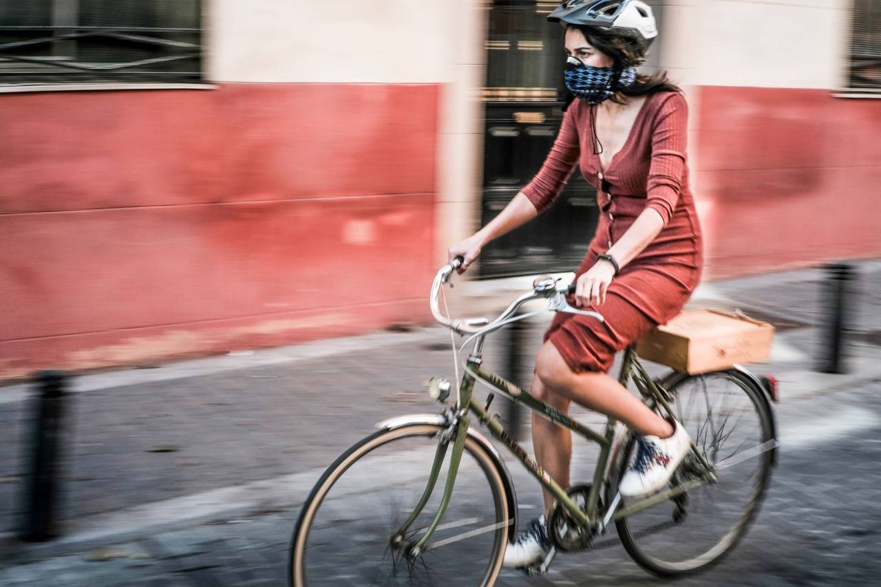 Una mujer circulando en bicicleta con mascarilla y casco.