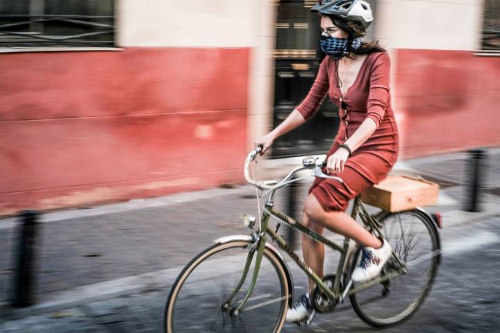 Una mujer circulando en bicicleta con mascarilla y casco.