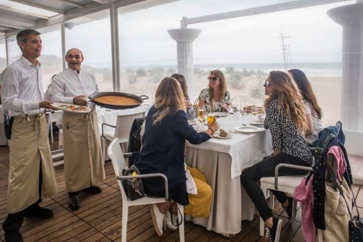 Unos camareros traen la paella a un grupo de amigas en el restaurante 'Arrocería Duna', en El Saler (Parque Natural de La Albufera, Valencia).