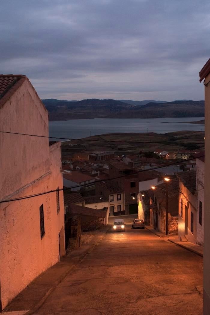 Calles desiertas al caer la noche en Peñalsordo, con el pantano al fondo.