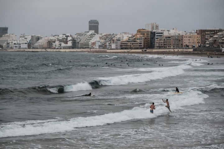 Varias personas bañándose en la Playa de Las Canteras con la ciudad al fondo.