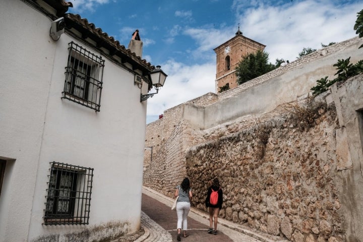 Dos personas caminan por una calle de Chinchón con la Torre del Reloj al fondo.