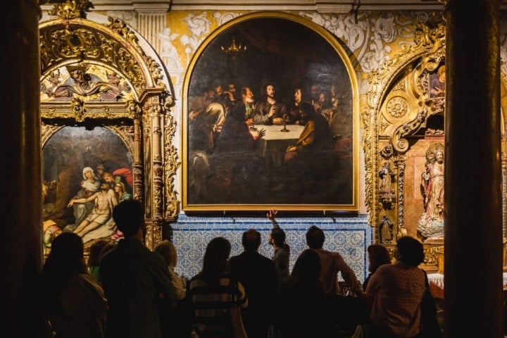 Un guía explica el cuadro de La Santa Cena de Murillo en la iglesia barroca de Santa María La Blanca durante la visita nocturna.