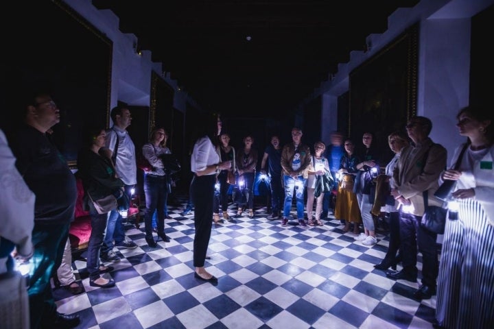 La guía de Engranajes Culturales recibe a los visitantes a la entrada del Hospital de la Caridad durante la visita nocturna, en Sevilla.