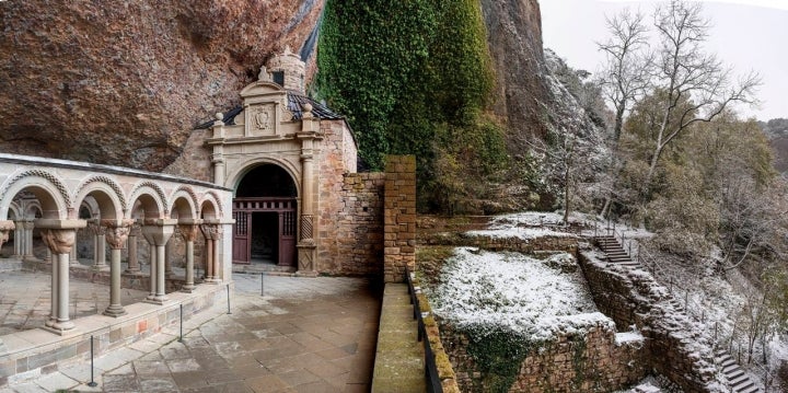 El claustro románico techado por la roca que sujeta una malla de alambre.