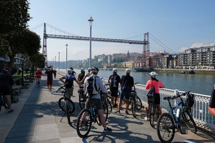 Un grupo de ciclistas observan el Puente Colgante cerca del monumento a Evaristo Churruca, en Getxo (Vizcaya).