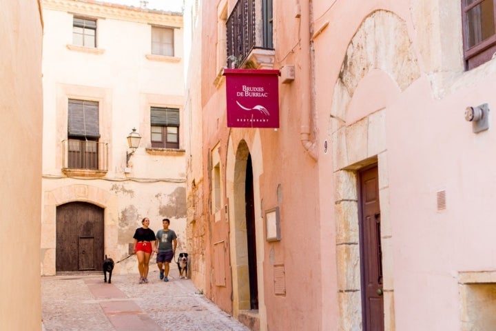 Una pareja y sus perros pasean junto al restaurante 'Bruixes de Burriac', en Carrer del Cup.