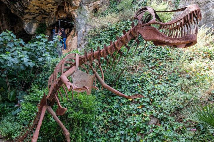 El esqueleto de metal de un dinosaurio a la entrada de la cueva.